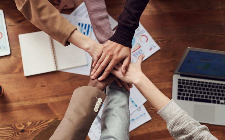 Diverse group huddled over a wooden table.