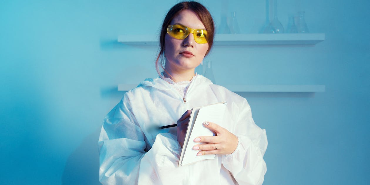 A researcher wearing a lab coat while holding a notebook.