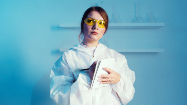 A researcher wearing a lab coat while holding a notebook.